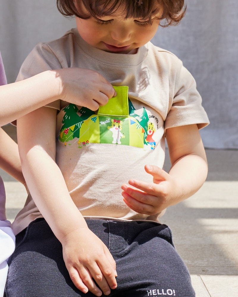 しまじろう　遊べるTシャツ（ベージュ）を着用してTシャツのプリントを見ている男の子の写真