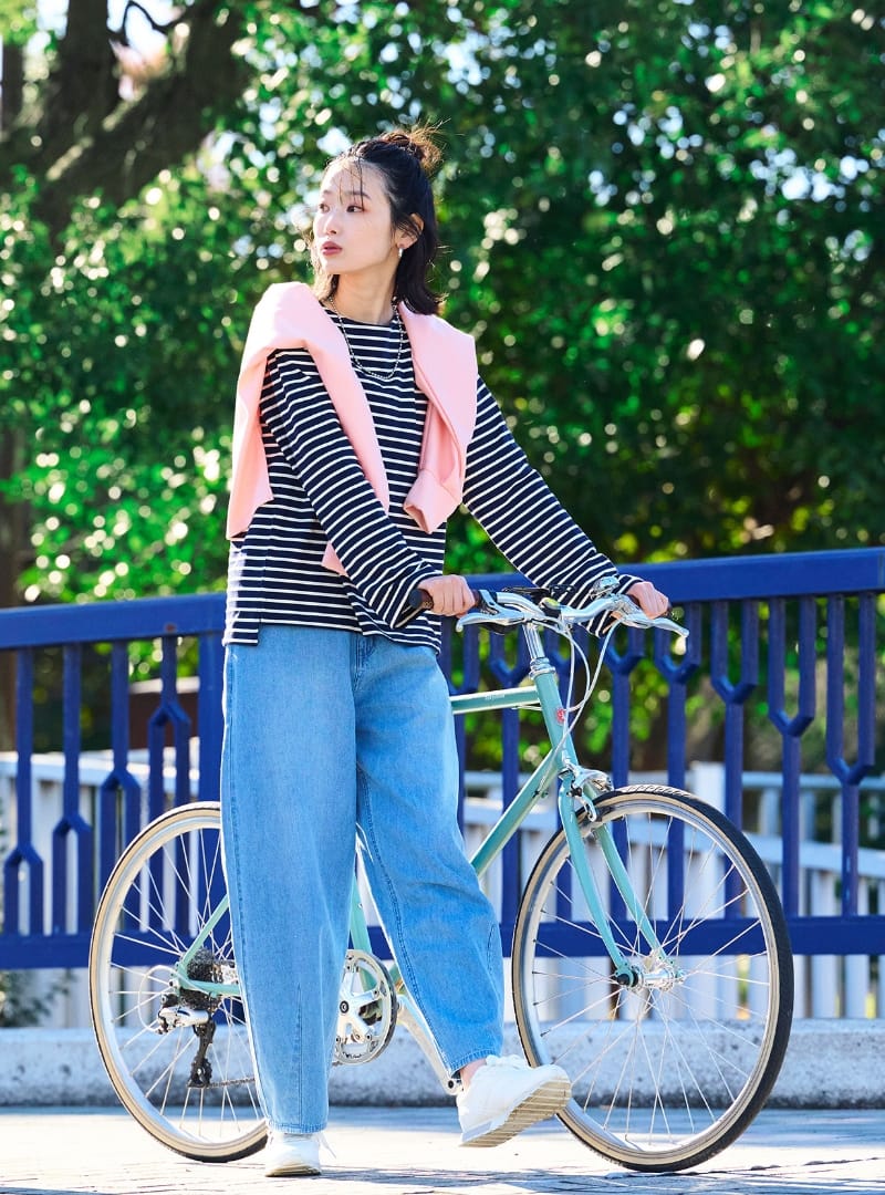 ボーダーの服を着てピンクの洋服を肩にかけた女性が自転車を押している画像