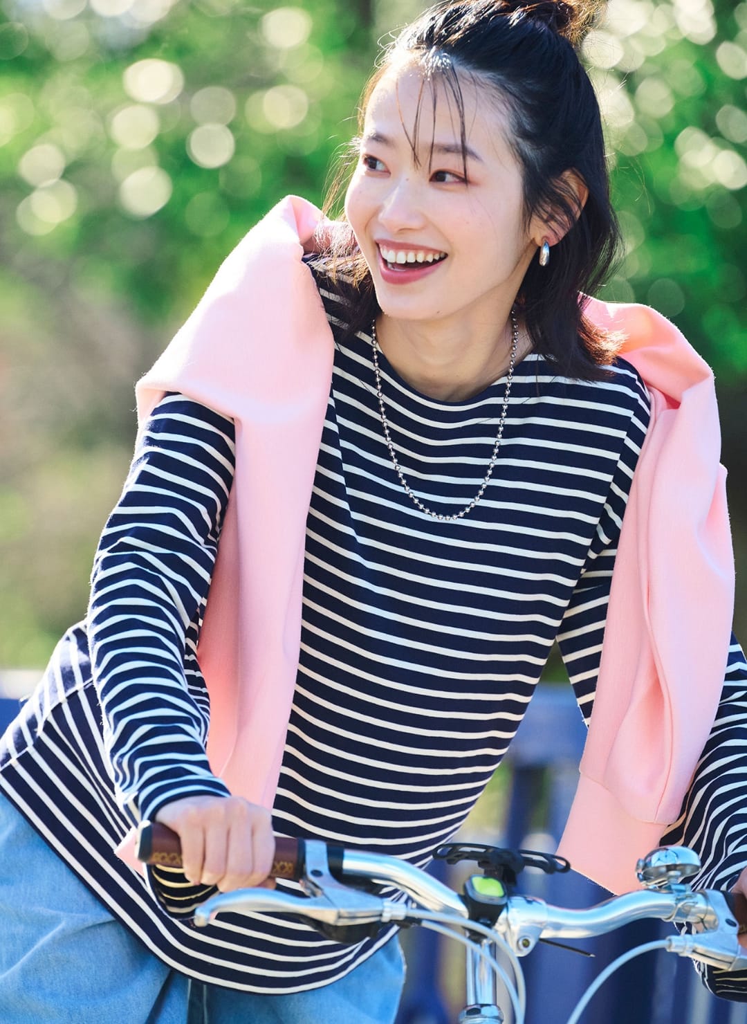 ボーダーの服を着てピンクの洋服を肩にかけた女性が自転車を押している画像